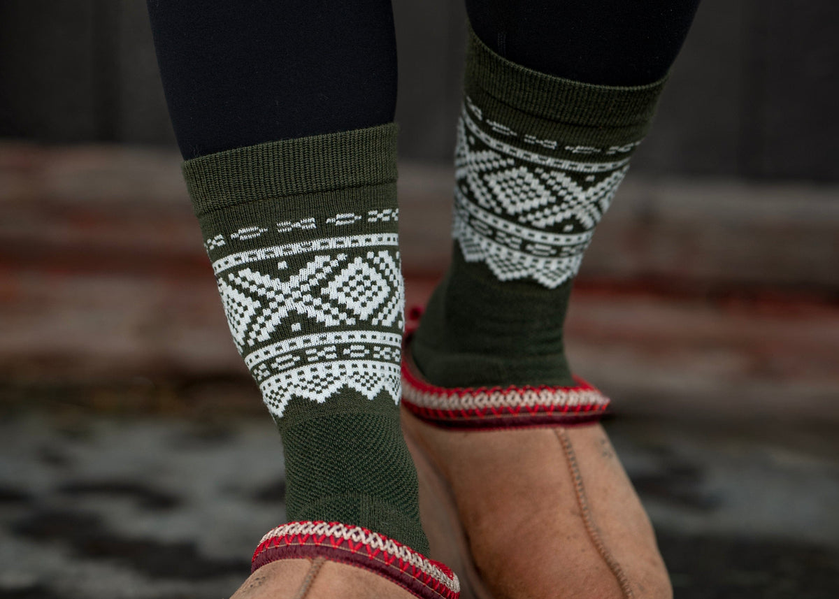 Person wearing green patterned socks with brown UGG boots on a dark surface